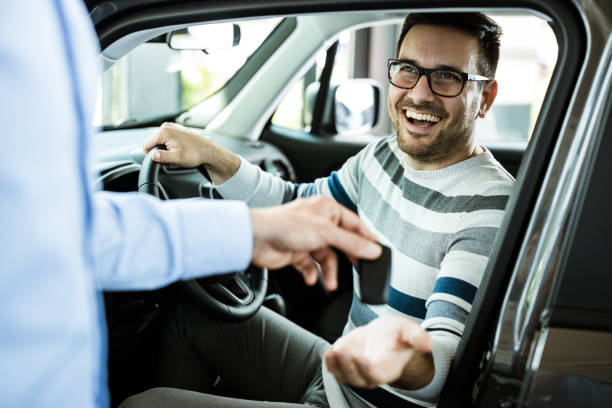 Young happy man receiving new car keys in a showroom. Happy man receiving keys for his new car in a showroom. car salesperson stock pictures, royalty-free photos & images