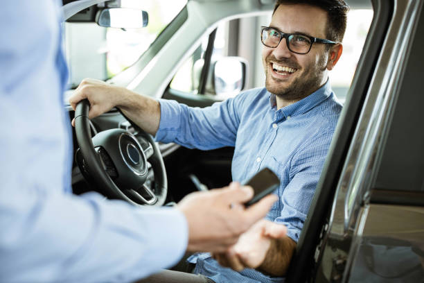 Young happy man receiving new car keys in a showroom. Happy man receiving keys for his new car in a showroom. car rental stock pictures, royalty-free photos & images