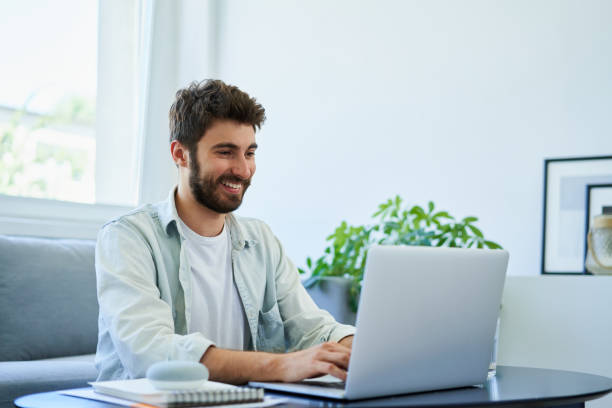 Young happy man typing on laptop while working at home. Good posture concept stock photo