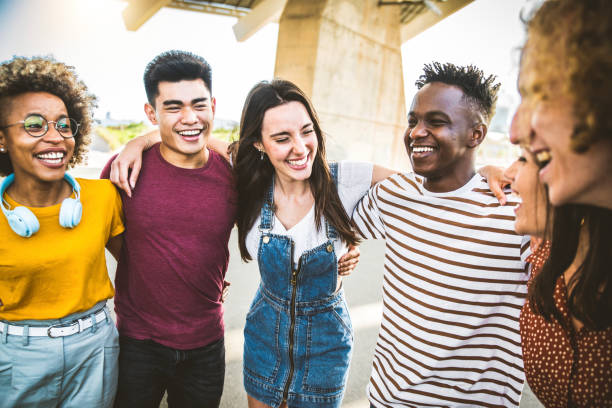 Young happy people laughing together - Multiracial friends group having fun on city street - Diverse culture students portrait celebrating outside - Friendship, community, youth, university concept stock photo