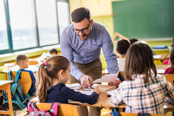 Young happy professor assisting his elementary students on a class at school. Young male teacher assisting his students on a class at elementary school. elementary age stock pictures, royalty-free photos & images