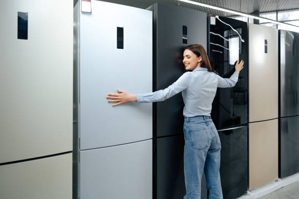 Young happy woman leaning on her new refrigerator in a mall stock photo