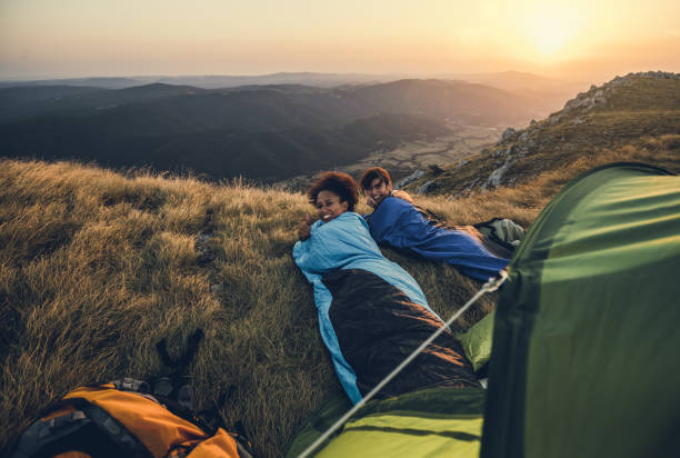 Jóvenes excursionistas acampando en la cima de la colina Jóvenes excursionistas acampando en la cima de la colina saco de dormir fotografías e imágenes de stock