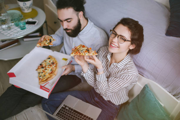 Young hipster male female couple home eating pizza with laptop stock photo