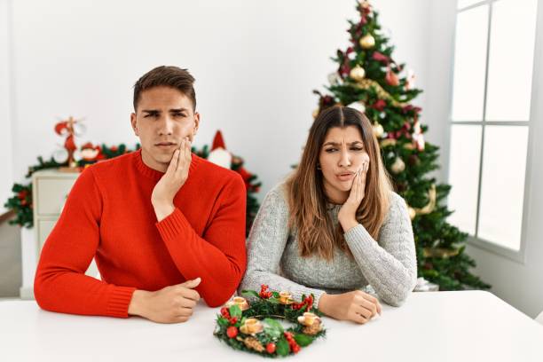 Young hispanic couple sitting at the table on christmas touching mouth with hand with painful expression because of toothache or dental illness on teeth. dentist stock photo