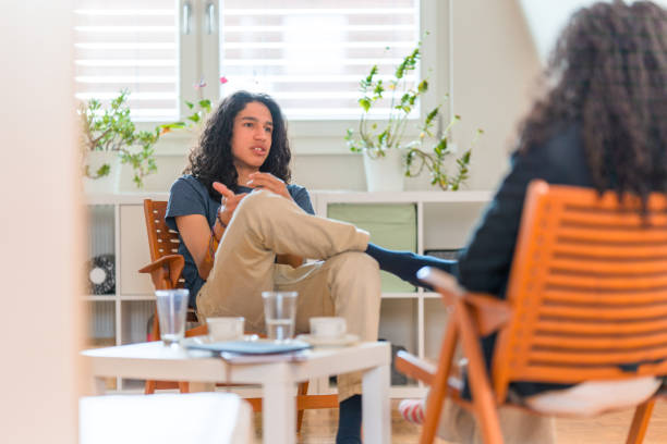 Young Hispanic Male Patient Listening To Female Psychotherapist in her Office stock photo