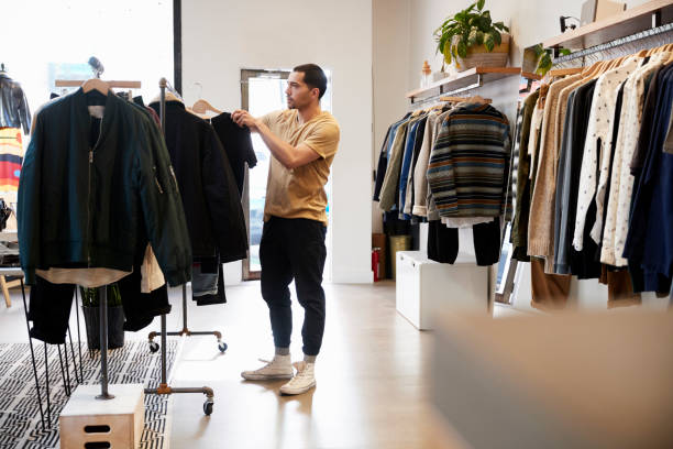 Young Hispanic man looking at clothes on a rail in a shop Young Hispanic man looking at clothes on a rail in a shop clothes rack stock pictures, royalty-free photos & images