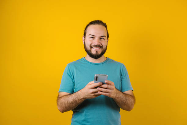 Young hispanic man using mobile phone on yellow background in Mexico Latin America stock photo