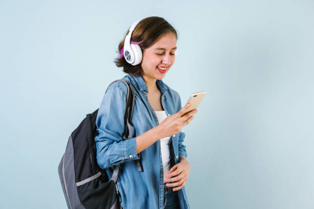 Young Hispanic student woman listen music with headphones using phone over isolated blue background stock photo