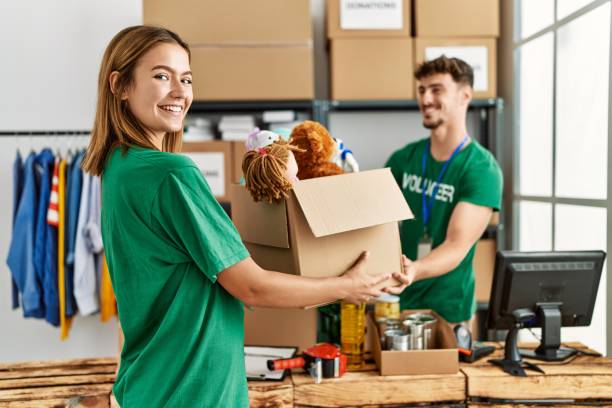 Young hispanic volunteer couple smiling happy giving box with toys to donate at charity center. stock photo