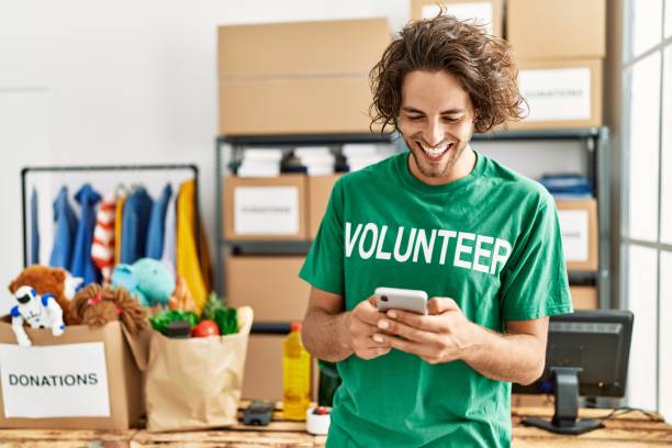 Young hispanic volunteer man smiling happy using smartphone at charity center. stock photo