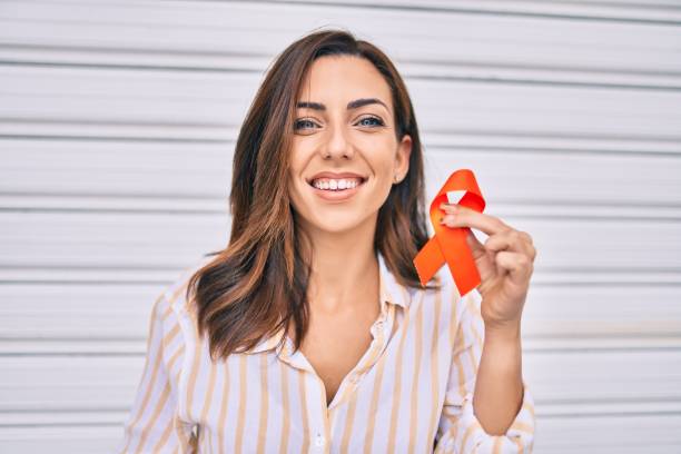 Young hispanic woman smiling happy holding awareness orange ribbon standing at the city. stock photo