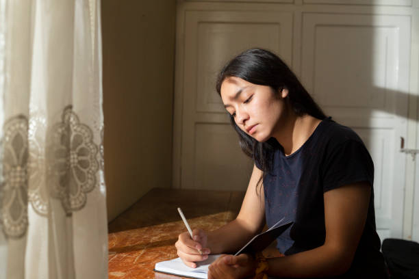 Young Hispanic woman writing in a notebook, serious girl writing in her journal in her room at sunset. concentrated young woman studying at home Young Hispanic woman writing in a notebook beautiful peruvian women stock pictures, royalty-free photos & images