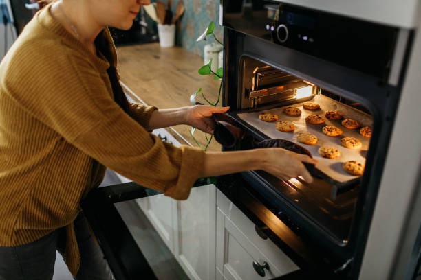Young home chef putting a tray full of cookies out of the oven stock photo