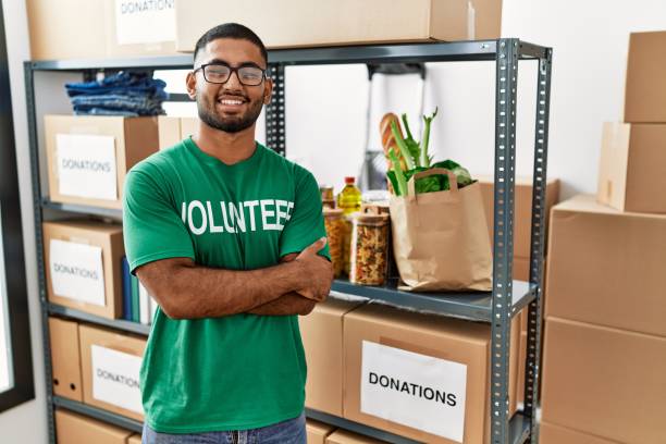 Young indian man volunteer holding donations box happy face smiling with crossed arms looking at the camera. positive person. stock photo