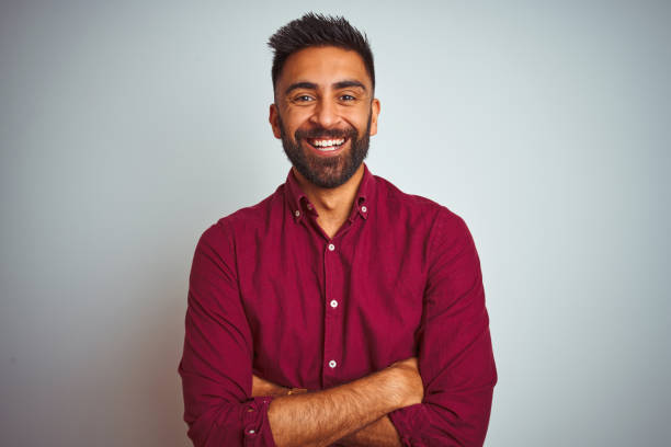 Young indian man wearing red elegant shirt standing over isolated grey background happy face smiling with crossed arms looking at the camera. Positive person. Young indian man wearing red elegant shirt standing over isolated grey background happy face smiling with crossed arms looking at the camera. Positive person. west asian ethnicity stock pictures, royalty-free photos & images