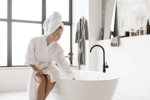 Young lady in bathrobe touching water Young lady in bathrobe touching water bathtub stock pictures, royalty-free photos & images