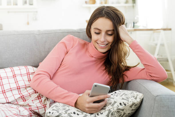年輕的女士躺在沙發上, 手裡拿著手機, 在網路聊天, 享受閒置時間 - free mobile chatting rooms 個照片及圖片檔