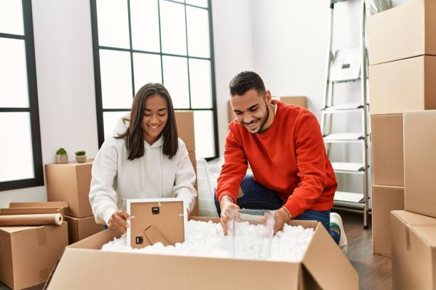 young latin couple smiling happy unboxing cardboard box at new home. - unbox stockfoto's en -beelden