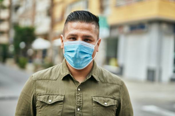 Young latin man wearing medical mask standing at the city. stock photo