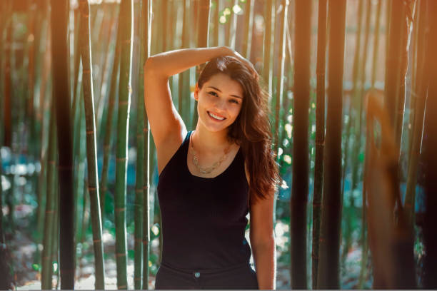 Young Latina woman smiling at the camera, in front of bamboo and sunlight coming form the background stock photo