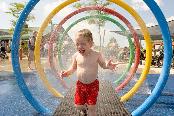 Young laughing boy runs through water park sprinklers stock photo