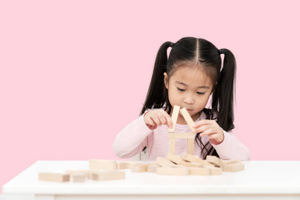 Young little cute asian girl build a house from wooden block construction, wood toy, jenga house on desk in isolated pink background. Asia children play and learn creative concept with copy space. Young little cute asian girl build a house from wooden block construction, wood toy, jenga house on desk in isolated pink background. Asia children play and learn creative concept with copy space. chinese girl hairstyle stock pictures, royalty-free photos & images