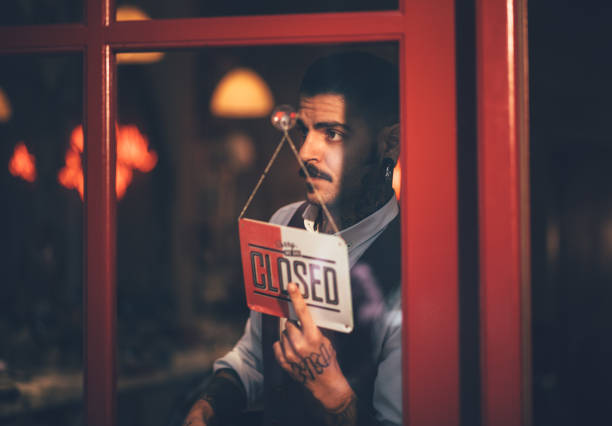 Young male business owner holding closed shop sign at window Young stylish man standing at barber shop door and closing business with closed signboard vintage beauty salon stock pictures, royalty-free photos & images