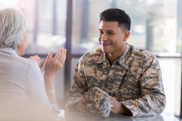 Young male in uniform smiles at counselor Young, adult, Hispanic male  smiles softy as his female counselor sitting across the table from him. She gestures as she speaks. veteran stock pictures, royalty-free photos & images