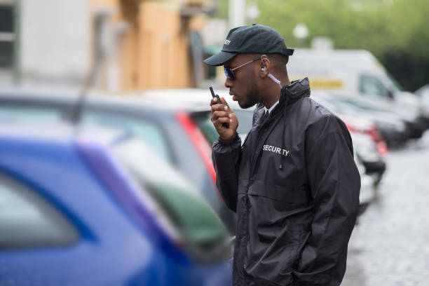 Young Male Security Guard Using Walkie-Talkie Young Male Security Guard In Black Uniform Using Walkie-Talkie On Street parking security guards stock pictures, royalty-free photos & images