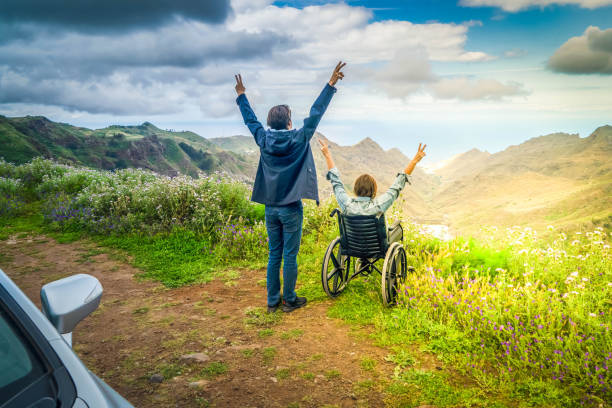 Young man and his wife in wheelchair travelling together by car in mountains stock photo