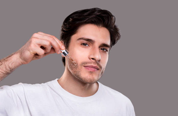 Young man applying organic essential serum on face Skin nutrition. Young man applying organic essential serum on face with pipette, free space mens cream stock pictures, royalty-free photos & images