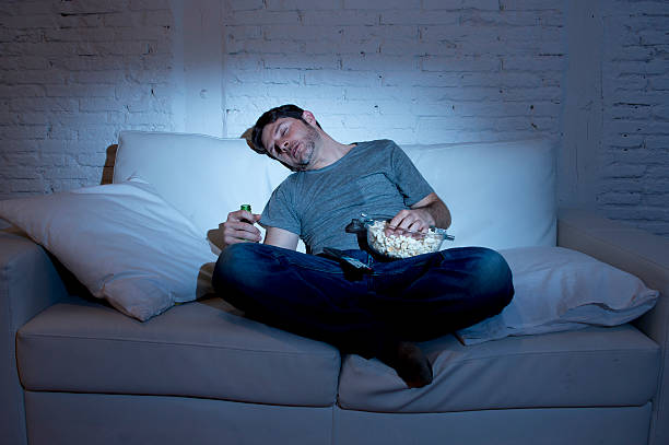 young man at home sofa sleeping while watching night television stock photo