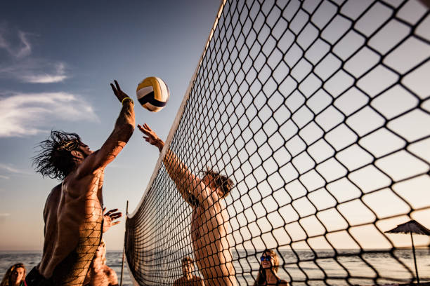 Young man blocking his friend while playing beach volleyball in summer day. Group of friends having fun while playing volleyball on the beach. One man is trying to block his friend. defending sport stock pictures, royalty-free photos & images