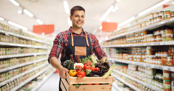 Young man carrying a crate with fresh vegetables in a supermarket stock photo