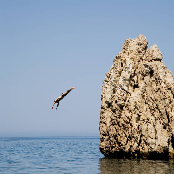 Young Man Cliff Diving into Ocean  cliff jumping stock pictures, royalty-free photos & images