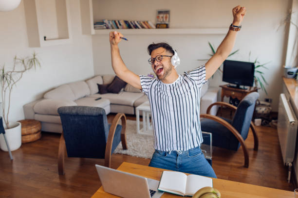 Young man dancing and singing after work at home Excited young man dancing and singing in front of his laptop at home. exhilaration stock pictures, royalty-free photos & images