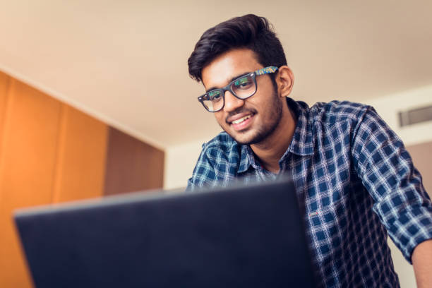 Young Man doing a Video Conferencing using his laptop Video Conference, Youth, Technology, Communication - Young Man standing casually in front of his laptop and talking to the WebCam indian ethnicity stock pictures, royalty-free photos & images