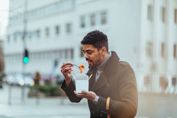 jeune homme mangeant la nourriture dans la rue - african america man eating chinese food photos et images de collection