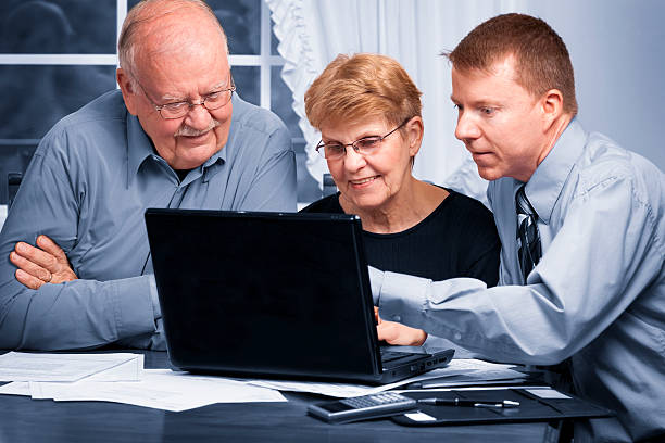 Young man explaining something on a laptop to senior couple stock photo