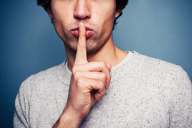 Young man gesturing hush with finger on lips stock photo