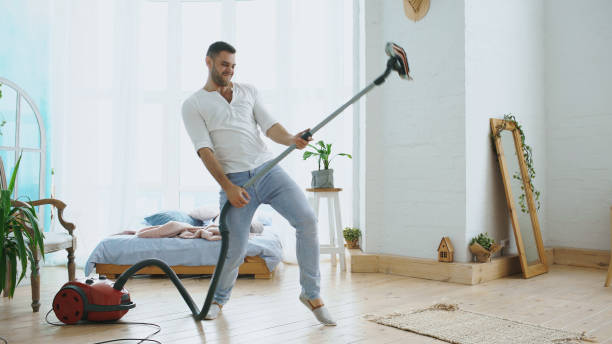 Young man having fun cleaning house with vacuum cleaner dancing like guitarist stock photo