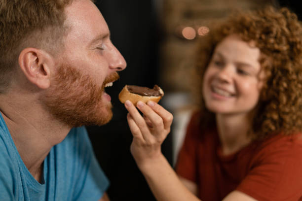 Young man having sweet breakfast with girlfriend. Close-up of young man being fed by girlfriend with bread and chocolate cream. couple eating chocolate stock pictures, royalty-free photos & images