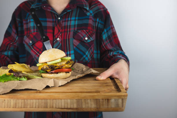 Young Man holding wooden cutting board with vegan burger and potato chips, wearing a vintage plaid shirt on white background. Vegan diet,vegetarian restaurant menu options Young Man holding wooden cutting board with vegan burger and potato chips, wearing a vintage plaid shirt on white background. Vegan diet,vegetarian restaurant menu options plant-based menu stock pictures, royalty-free photos & images