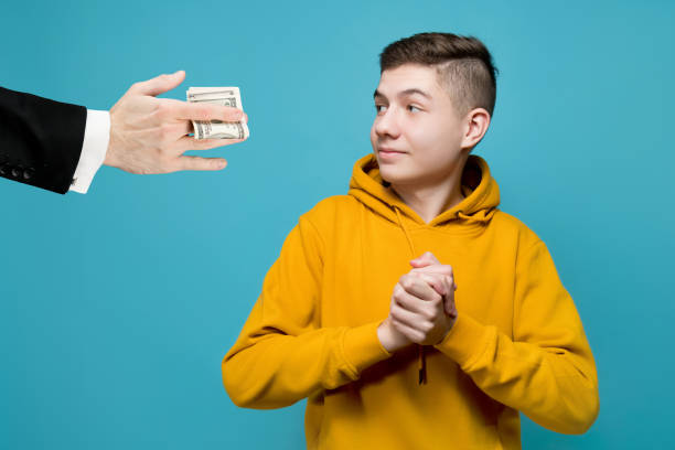 A young man in a bright sweatshirt rejoices that a business man gives him money A young man in a bright sweatshirt rejoices that a business man gives him money. Men's hands in jackets hold out dollars to a teenager, he smiles. The boy born with a silver spoon in his mouth allowance stock pictures, royalty-free photos & images
