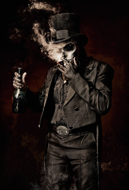 Young man in image of Baron Samedi, the Voodoo deity. Baron Saturday in black suit and top hat with a bottle of alcohol in hand. Day of the Dead (and Halloween) theme stock photo