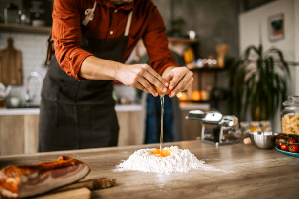 Young man in kitchen preparing dough for pasta stock photo
