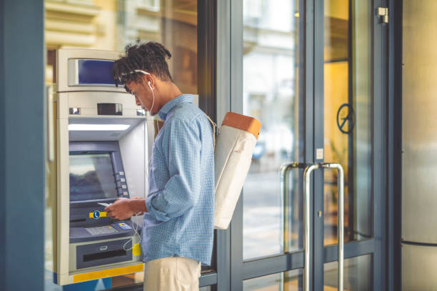 Young man is withdrawing money from an ATM Young man is withdrawing money from an ATM banks and atms stock pictures, royalty-free photos & images