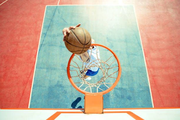 Young man jumping and making a fantastic slam dunk playing street ball, basketball. Urban authentic. stock photo