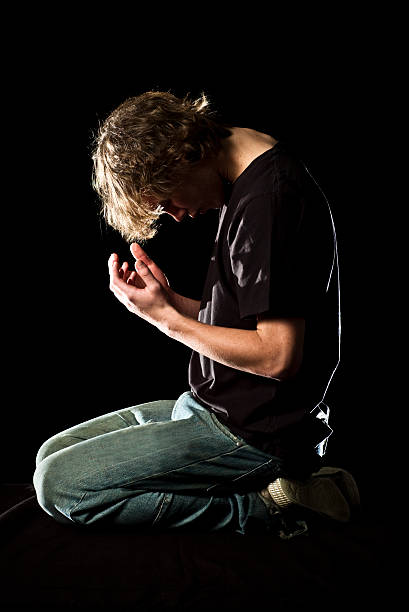 Young man kneels and prays stock photo
